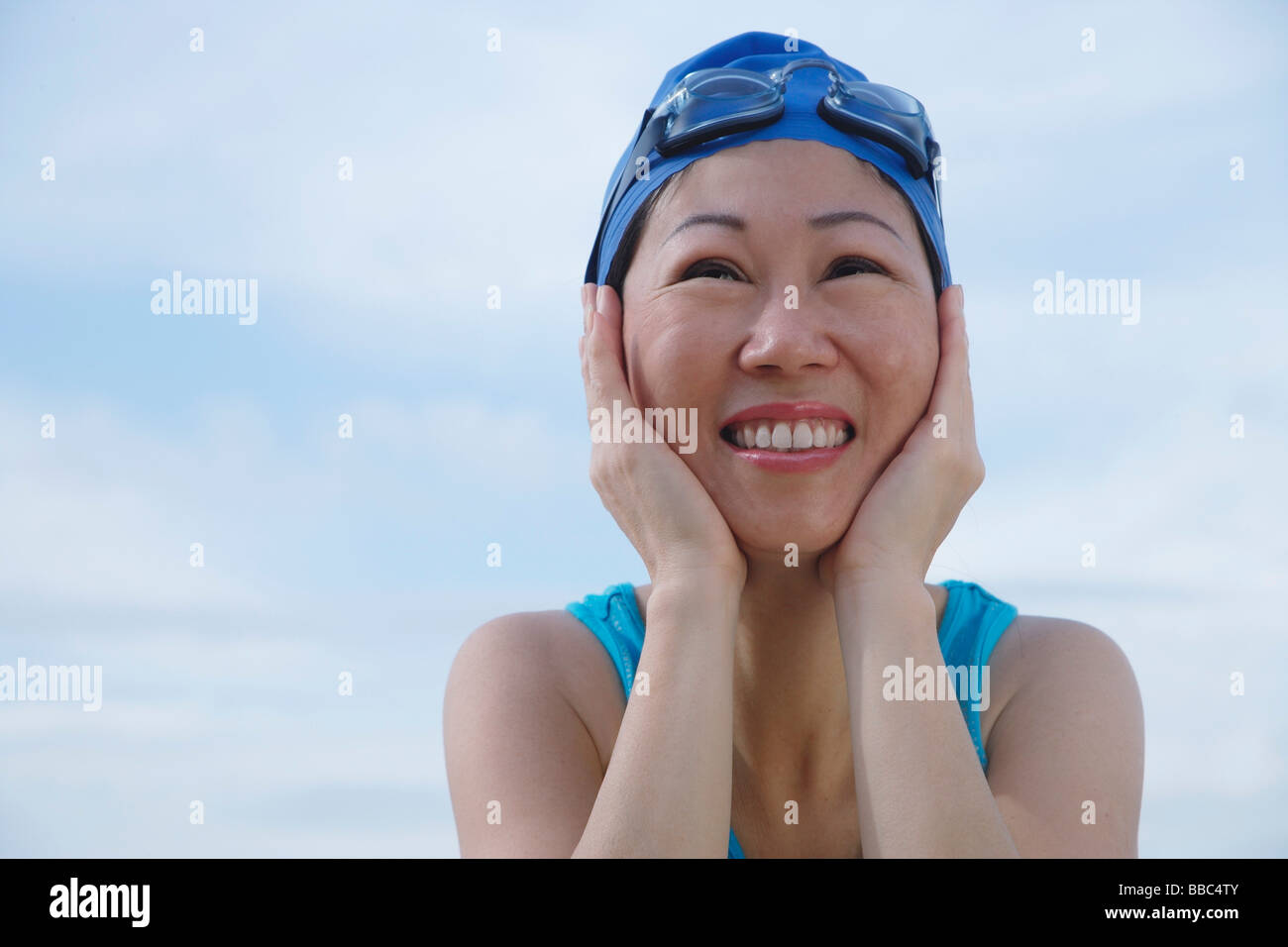 Mature woman wearing swim cap and goggles, hands on face, looking away