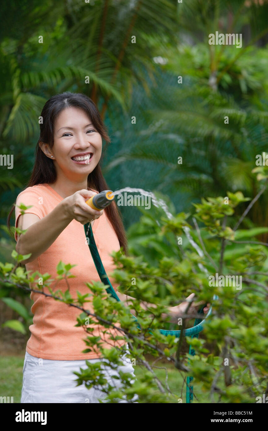 Woman watering plants in garden, smiling at camera Stock Photo - Alamy