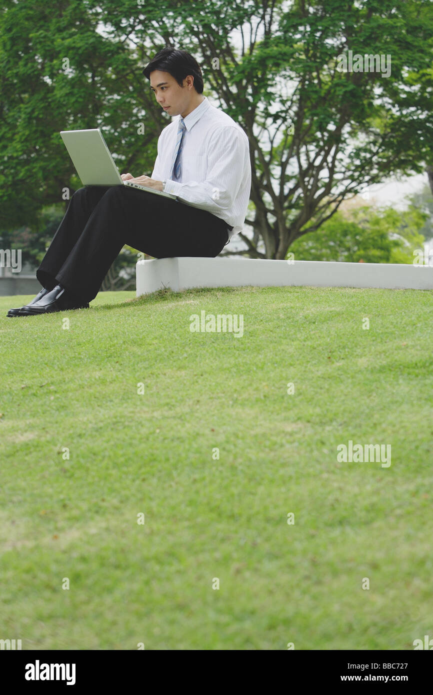 Businessman sitting in park using laptop Stock Photo - Alamy