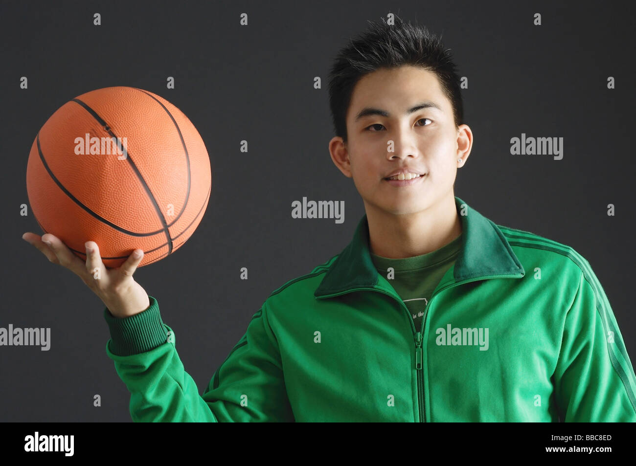 Young man wearing green tracksuit jacket, holding basketball Stock Photo