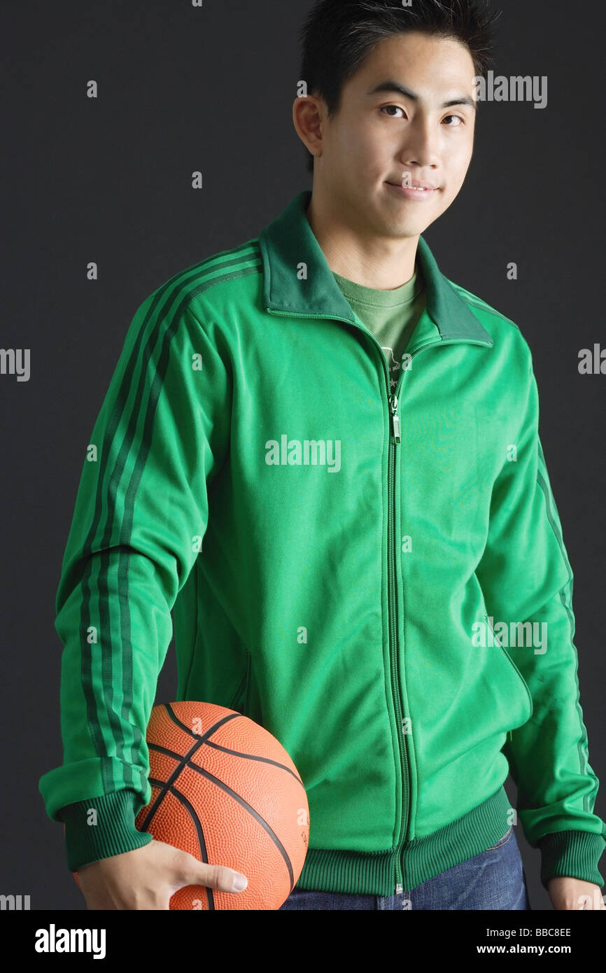Young man wearing green tracksuit jacket, holding basketball, looking at camera Stock Photo