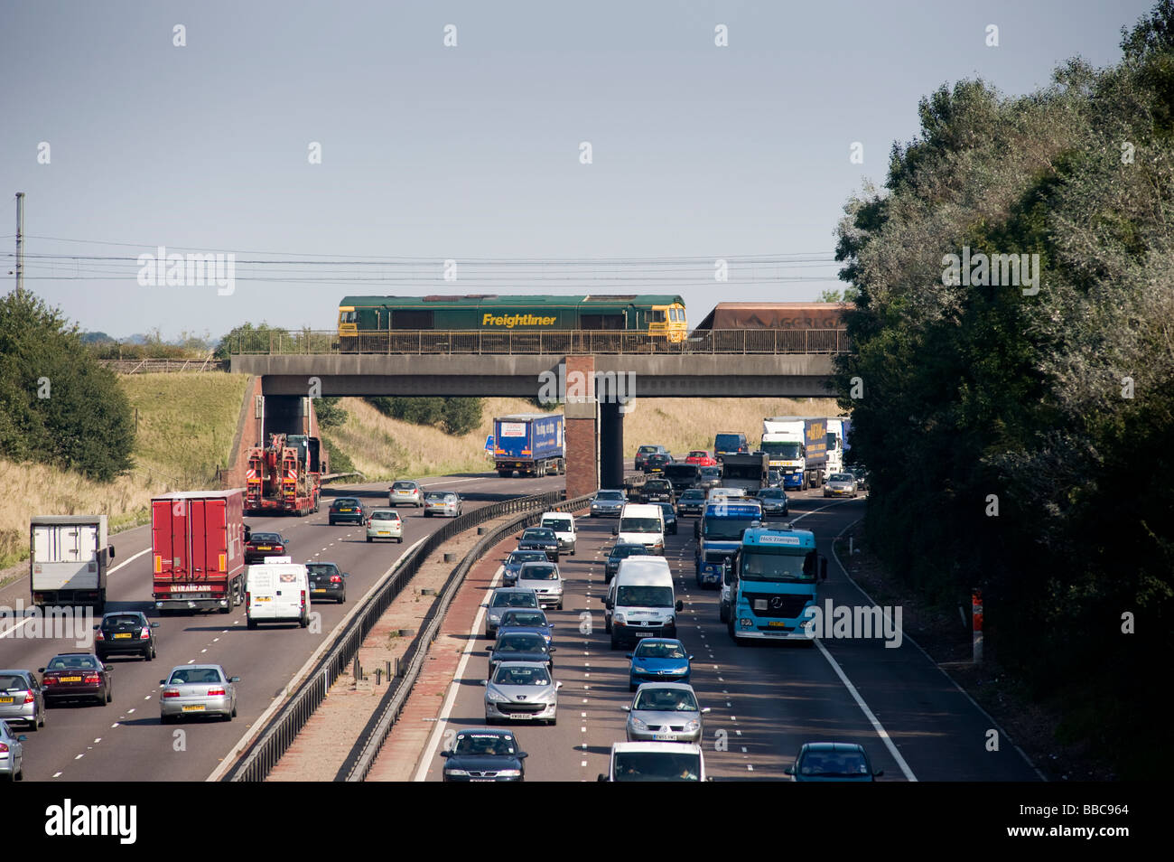 Freightliner locomotive hauling aggregate wagons across a bridge spanning a busy motorway in England Stock Photo