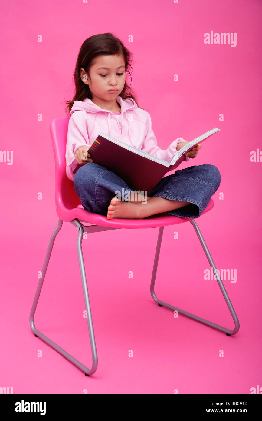 Girl on chair, reading a book, frowning Stock Photo