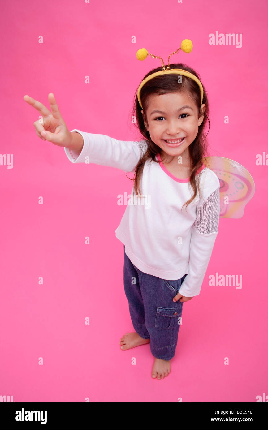 Young girl wearing fairy wings and deely bopper, making peace sign ...