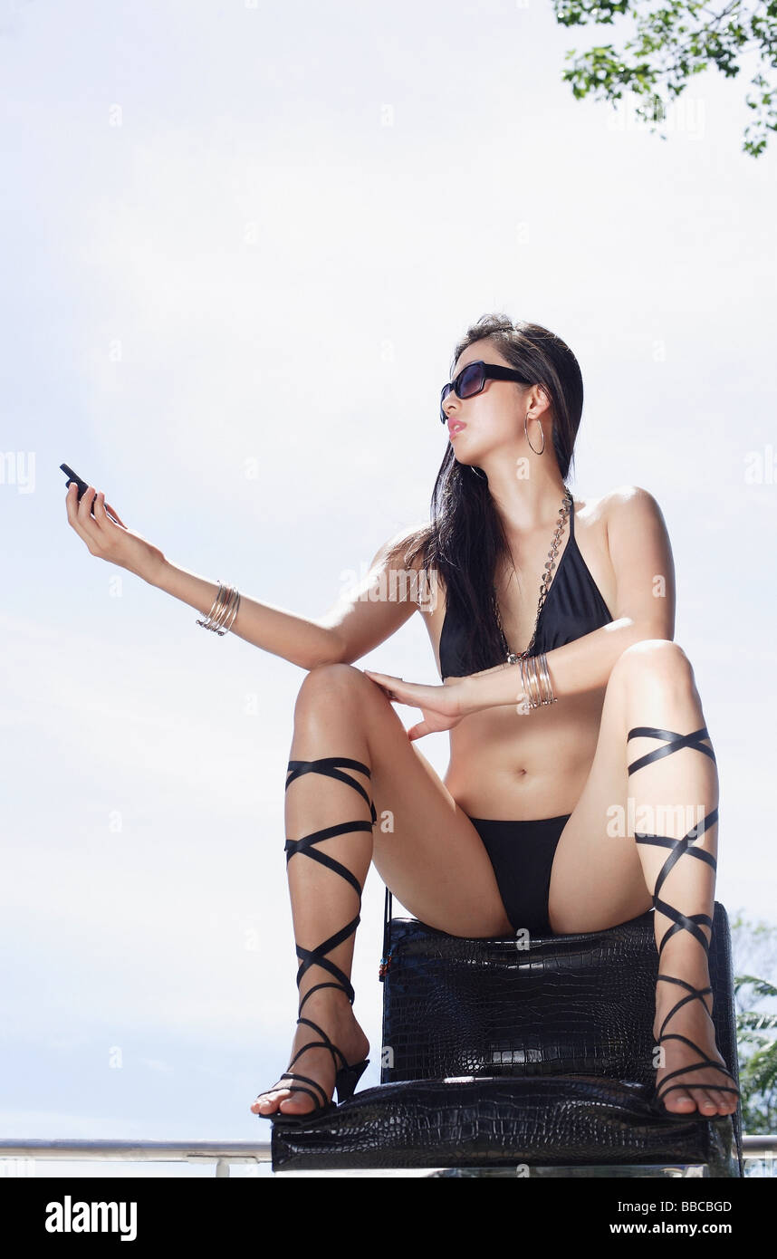 Woman in bikini and high heels, sitting in chair, holding mobile phone Stock Photo