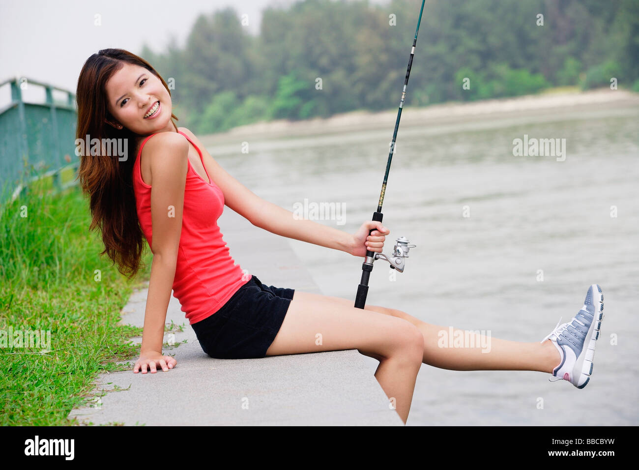 Woman sitting by river, holding fishing rod Stock Photo - Alamy