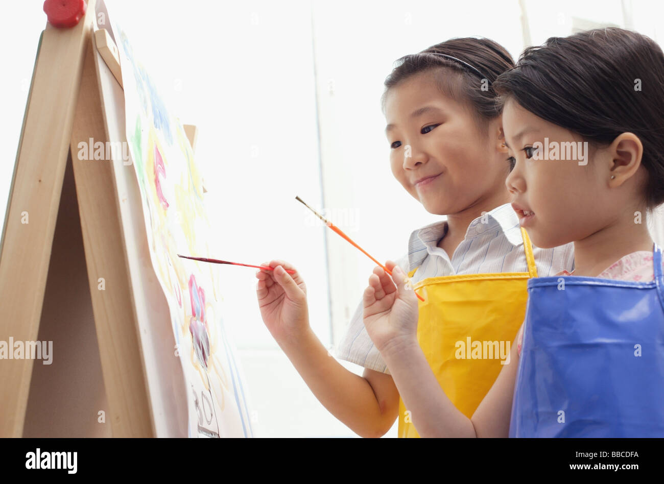 Young girls standing side by side, painting on easel Stock Photo - Alamy