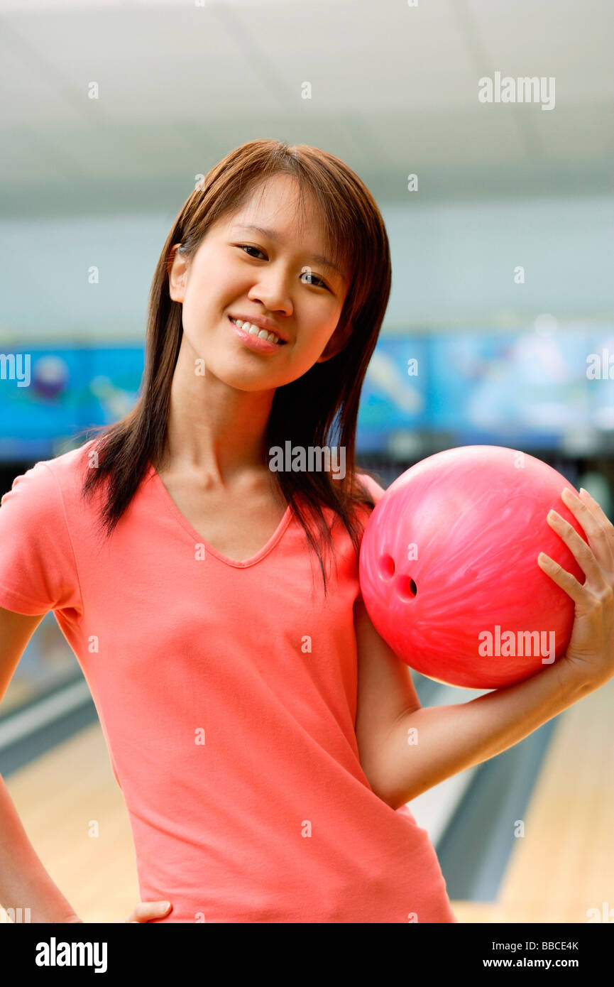 Woman at bowling alley holding bowling ball, hand on hip Stock Photo