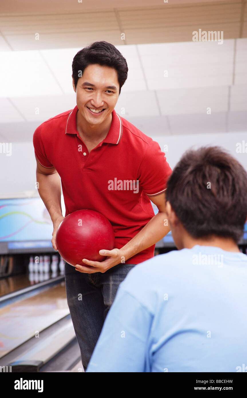 Man holding bowling ball, facing seated man Stock Photo Alamy
