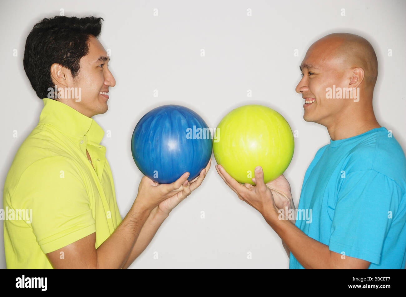 Two men standing face to face, carrying bowling balls, smiling Stock