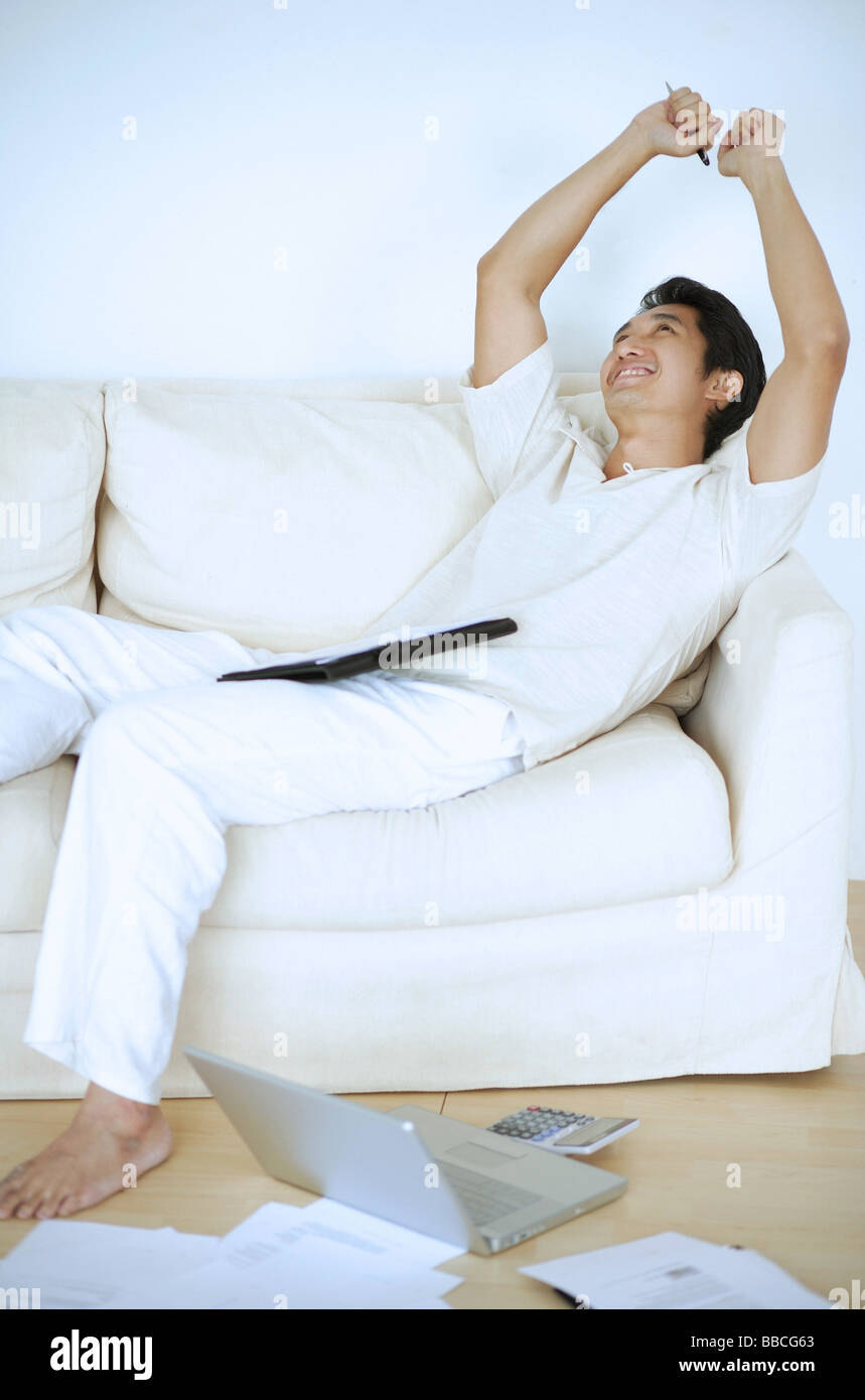Man lying on sofa, sleeping, arms raised, laptop and documents on floor