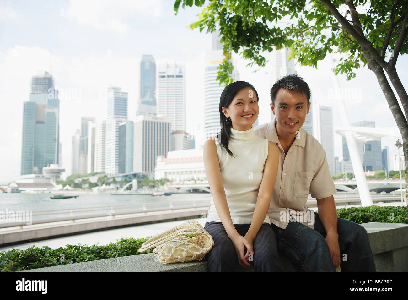 Young couple sitting on park bench, looking at camera Stock Photo - Alamy