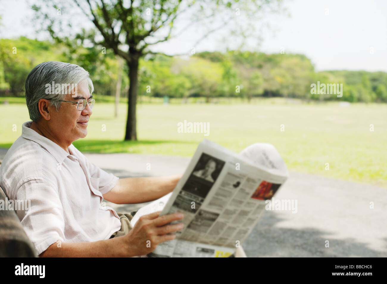 Senior man sitting in park reading newspaper Stock Photo - Alamy