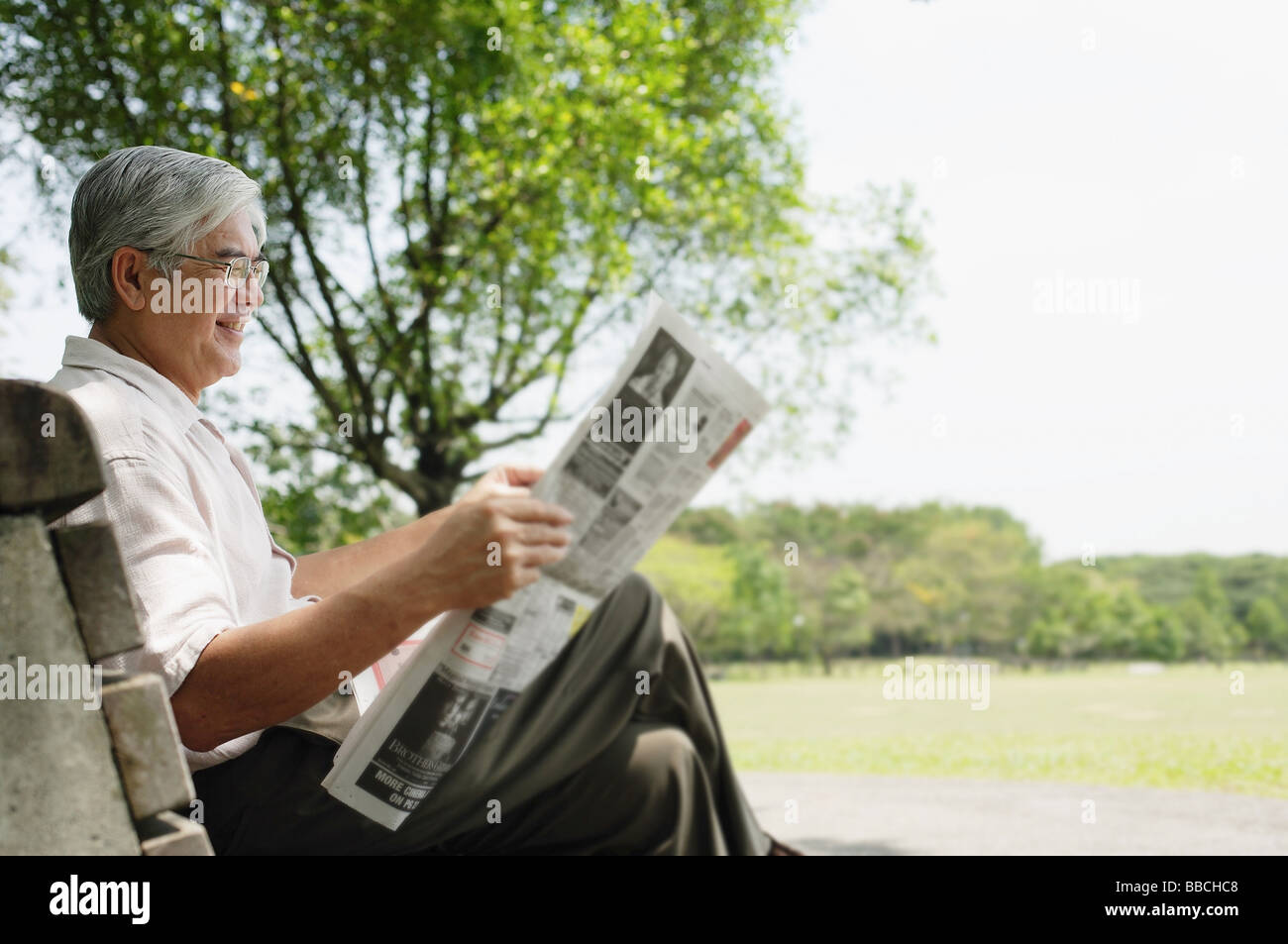 Senior man sitting on bench in park reading newspaper Stock Photo - Alamy