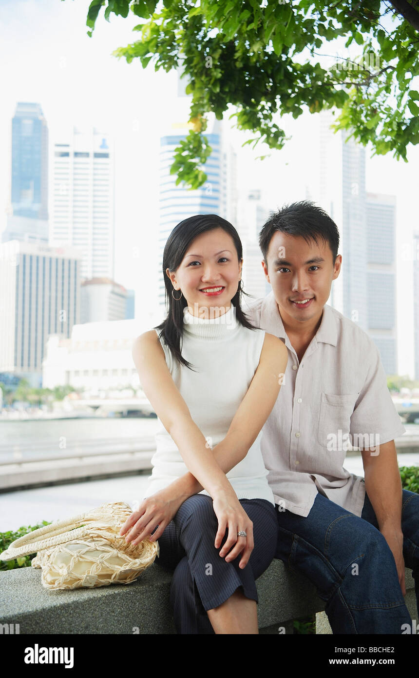 Young couple sitting on park bench, looking at camera Stock Photo - Alamy
