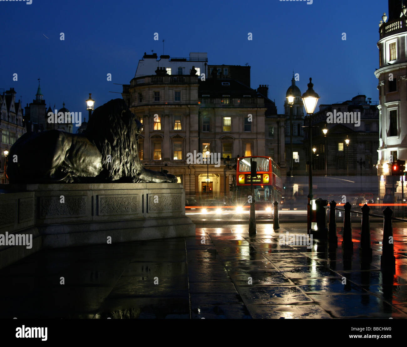 A sculpture of a lion watches traffic move around Trafalgar square on a wet winter evening  in London, England. Stock Photo