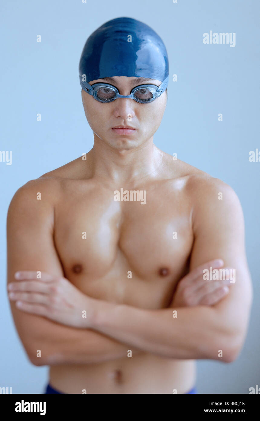 Man wearing swimming cap and goggles, arms crossed, looking at camera Stock Photo