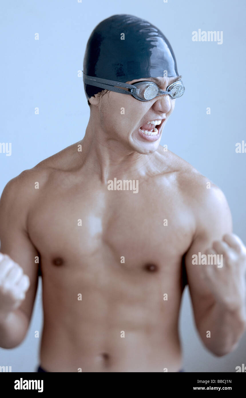 Man wearing swimming cap and goggles, making fists and grimacing Stock Photo