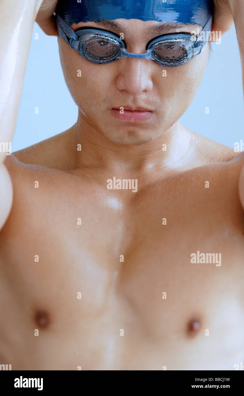 Man adjusting swimming cap, wearing goggles, looking at camera Stock Photo