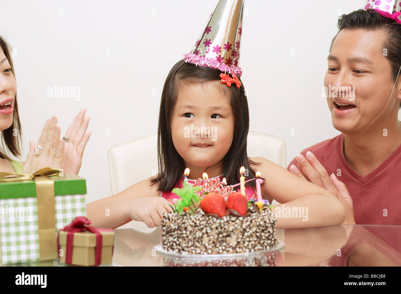 Girl with birthday cake, parents on either side clapping Stock Photo
