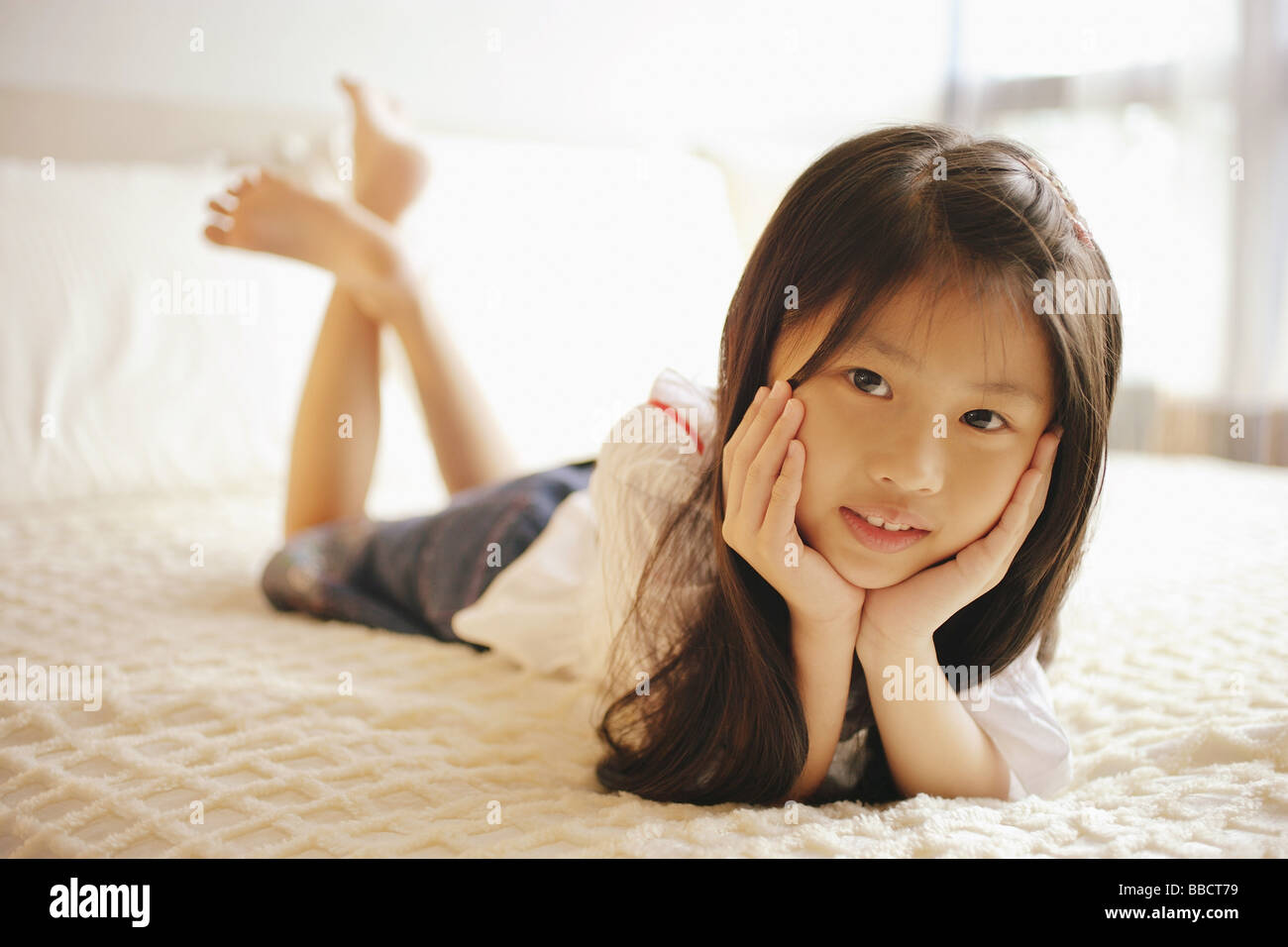 Young girl with hands on chin, lying on bed, looking at camera Stock