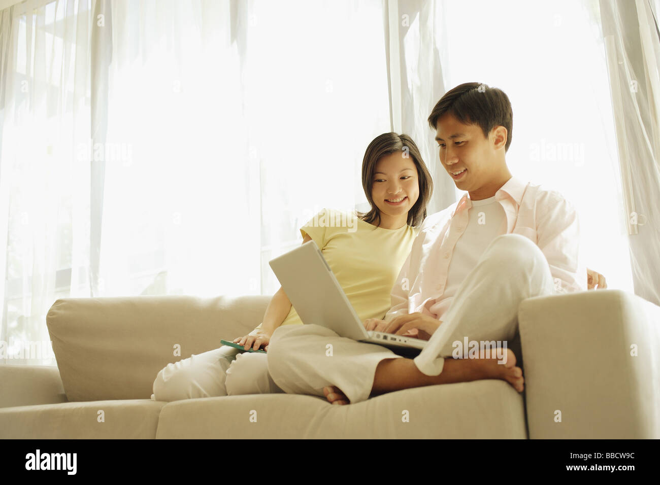 Young couple sitting on sofa side by side, using laptop Stock Photo - Alamy