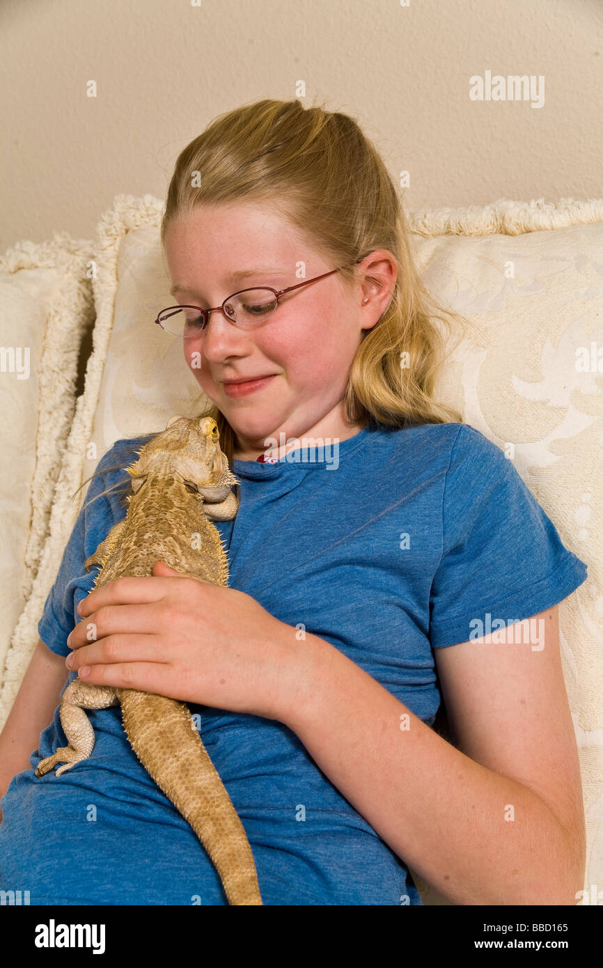 Portrait Young girl 9-11 year olds makes face bearded dragon climbing up on her Stock Photo