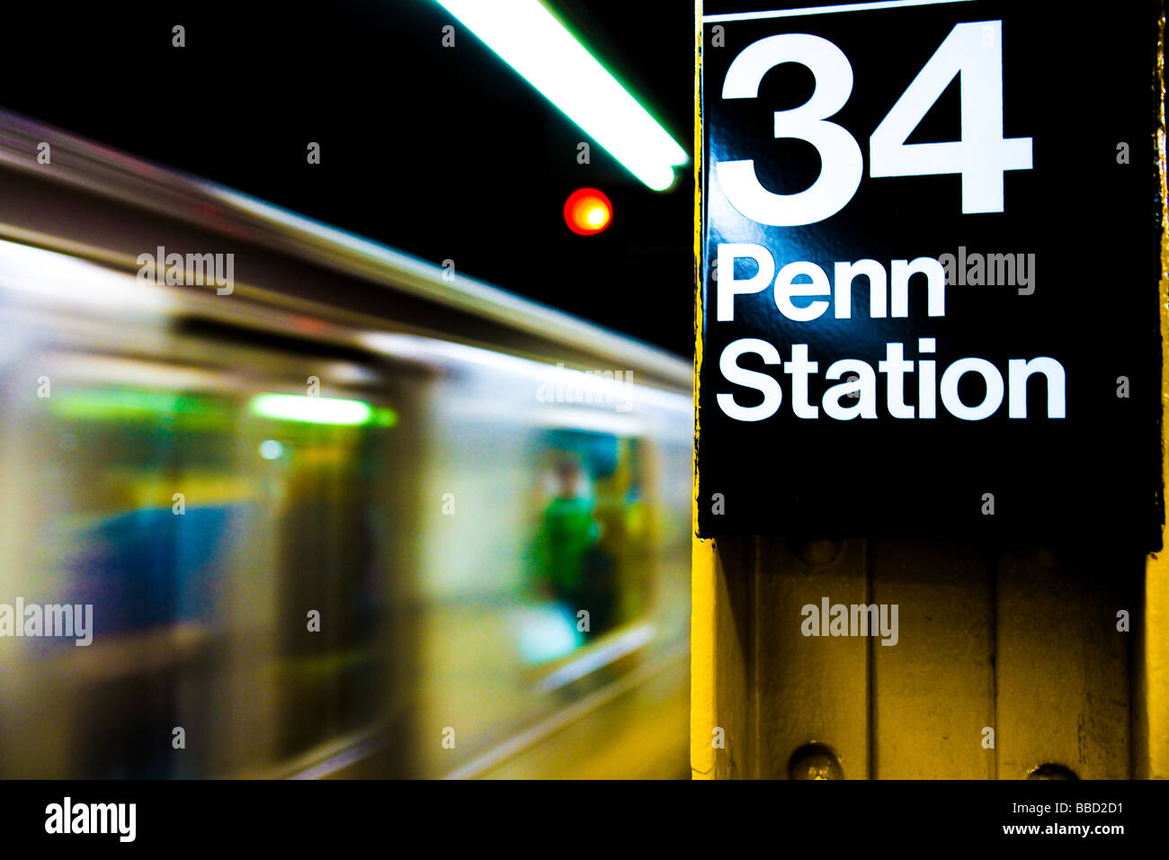 Motion-blurred train passing by a New York subway sign at platform of the city's 34th street Penn Station Stock Photo