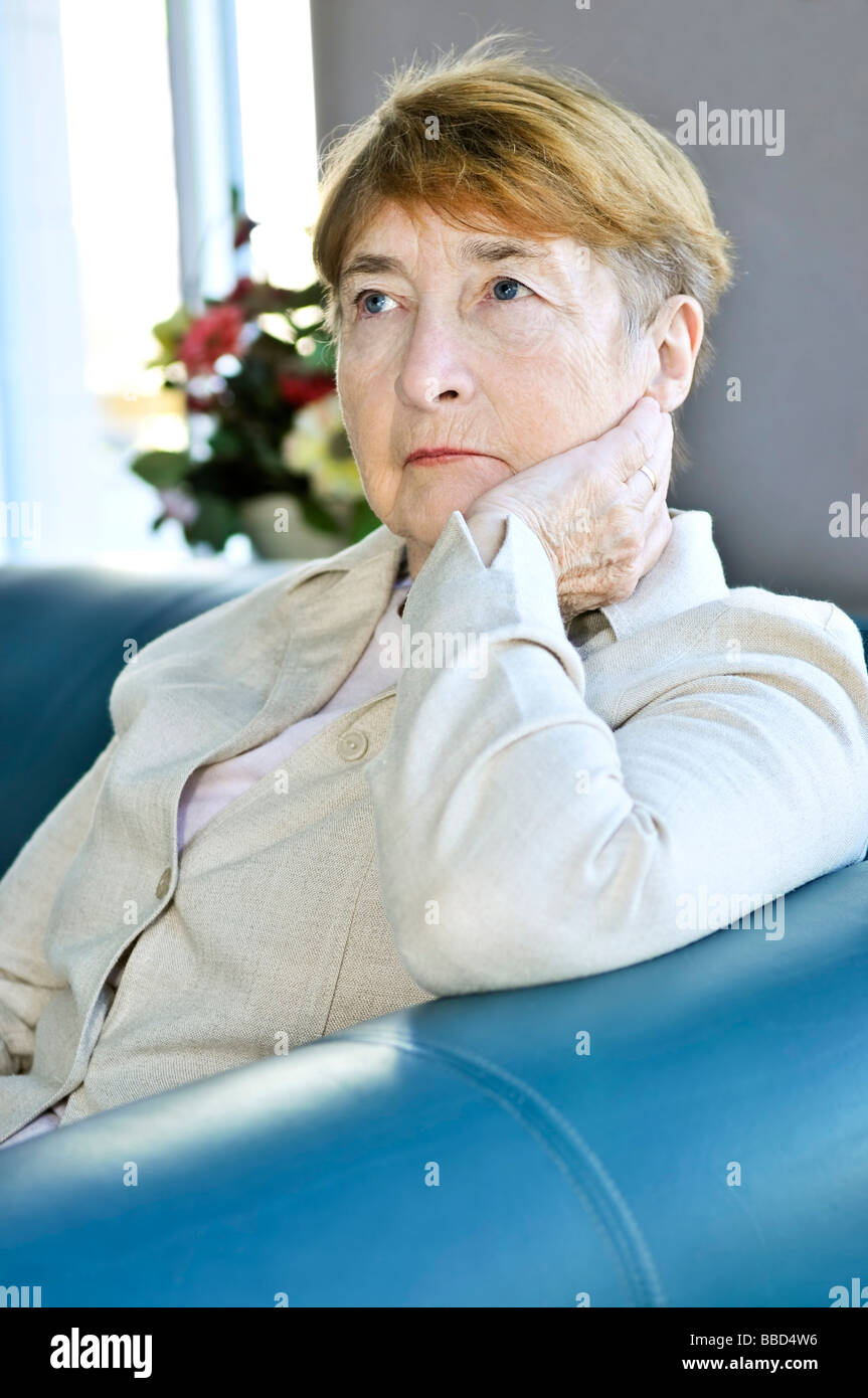 Sad elderly woman sitting on a couch indoors Stock Photo - Alamy
