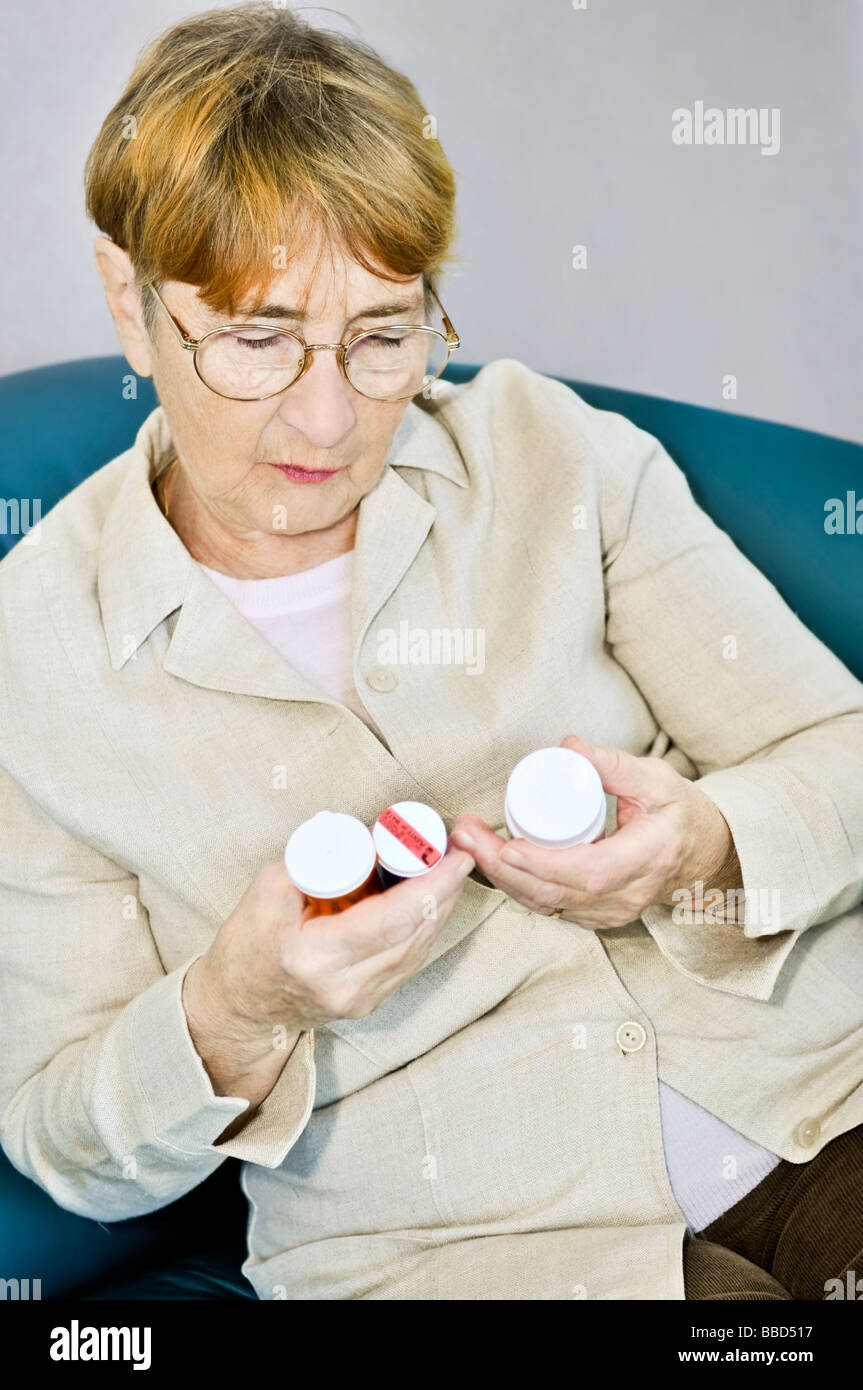 Elderly woman reading warning labels on pill bottles with medication Stock Photo
