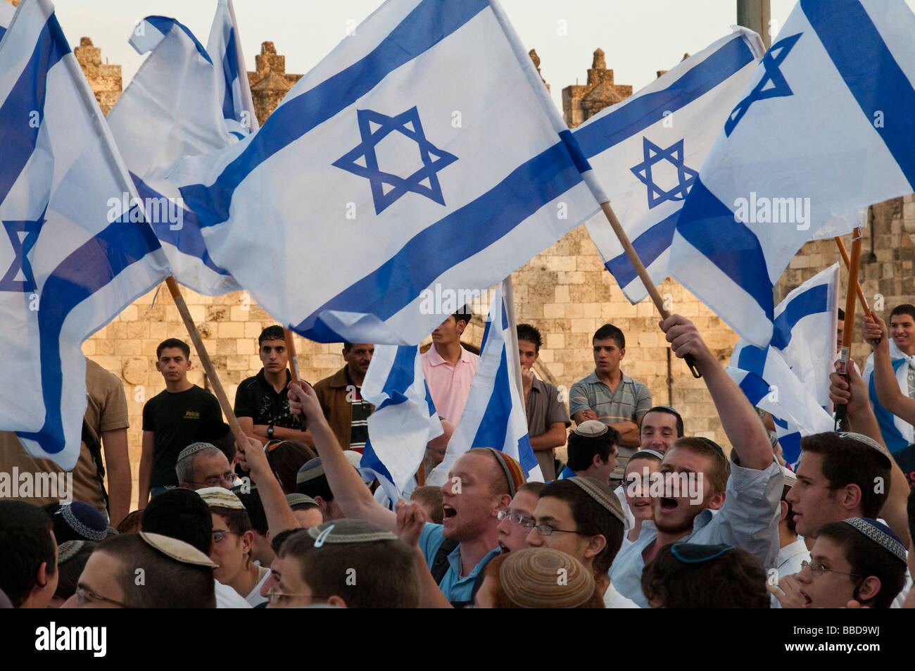 Israel Jerusalem Jerusalem day celebration Young religious israeli men marching with flags and Palestinian men watching Stock Photo