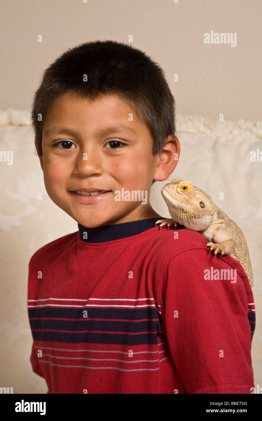 Portrait young 7-9 year old olds age Hispanic ethnicity boy Bearded Dragon on shoulder Looking at camera closeup light background cutout cut out Stock Photo