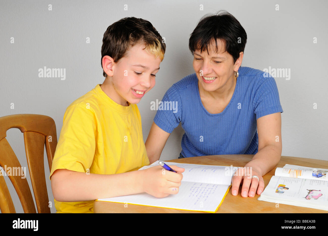 Boy doing homework for school, mother helping him, both laughing Stock Photo