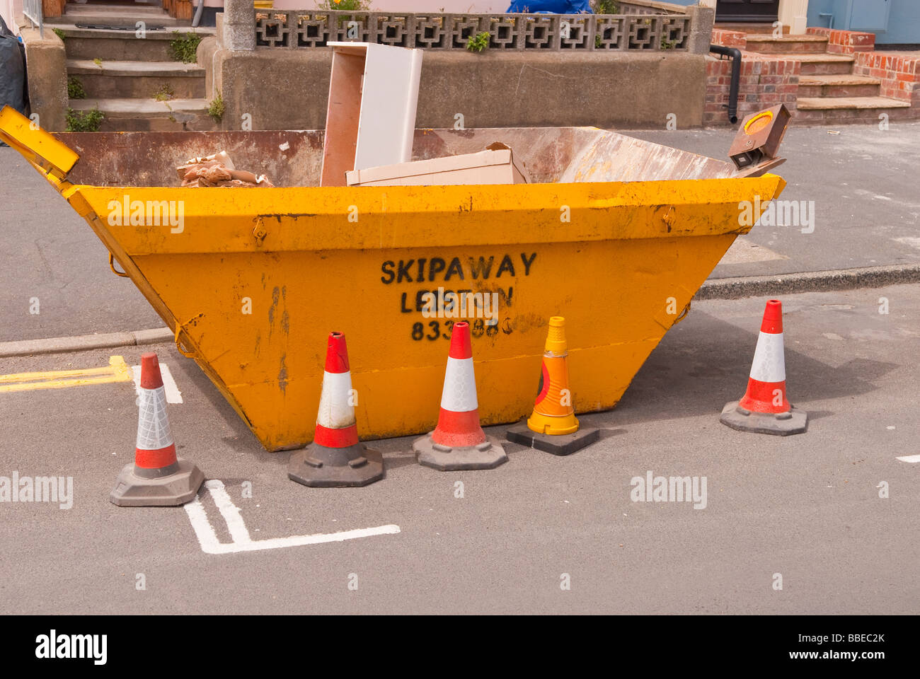 A builders rubbish skip in the street with traffic cones placed round