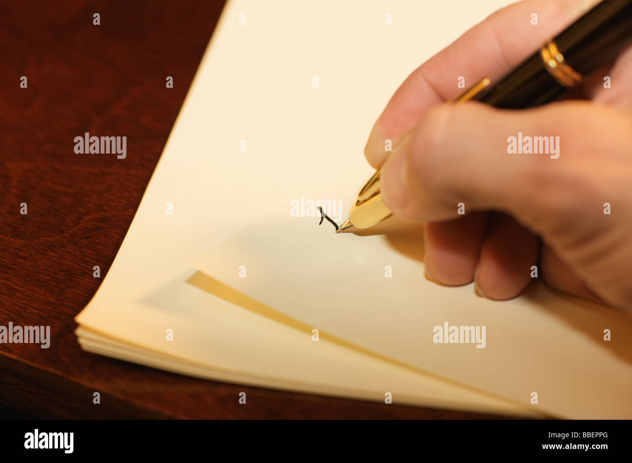 A hand writing on linen paper with a fountain pen on a wooden desk