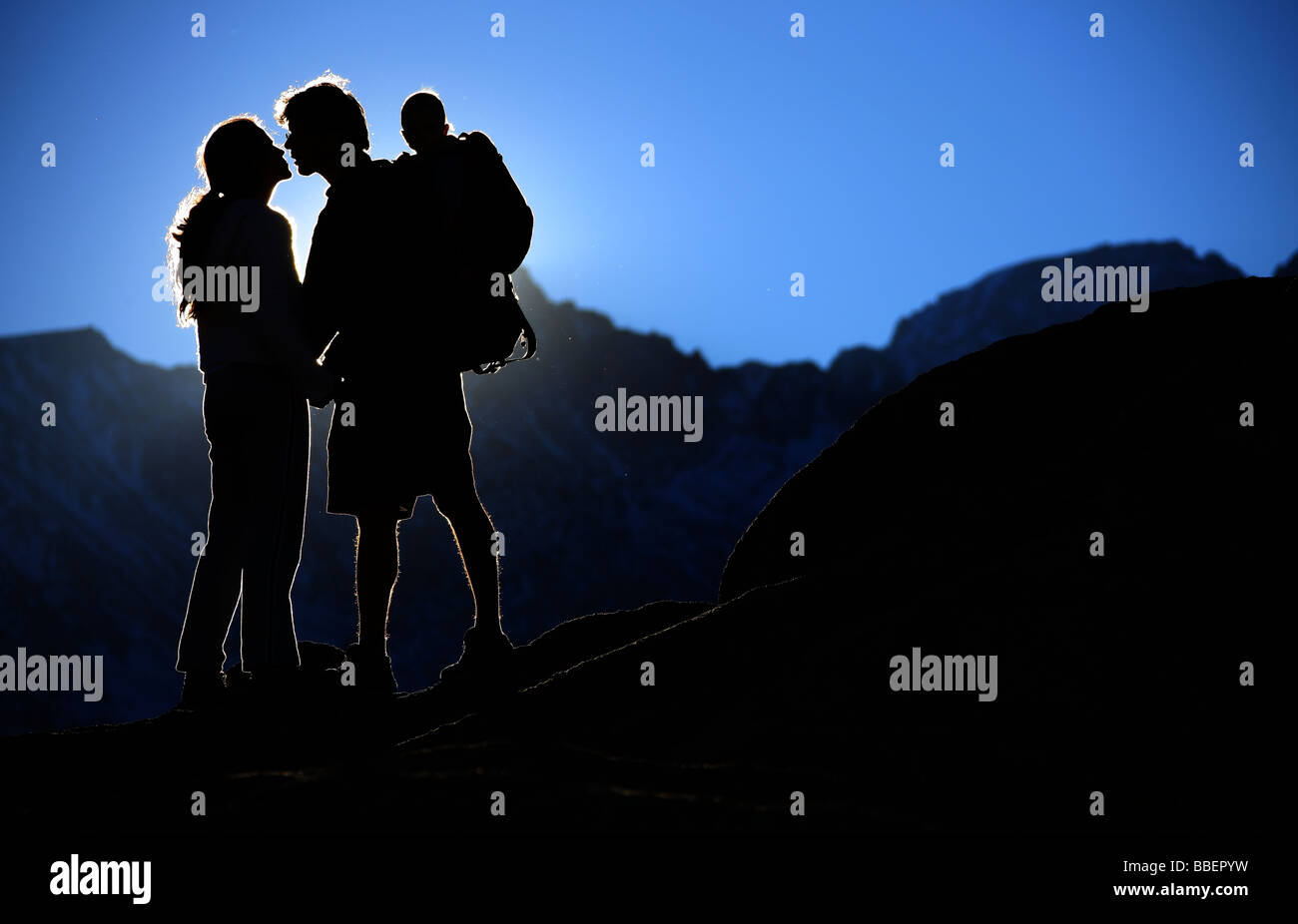 Young couple kissing in setting sun while carrying son on back,  Sierra Nevadas, California Stock Photo