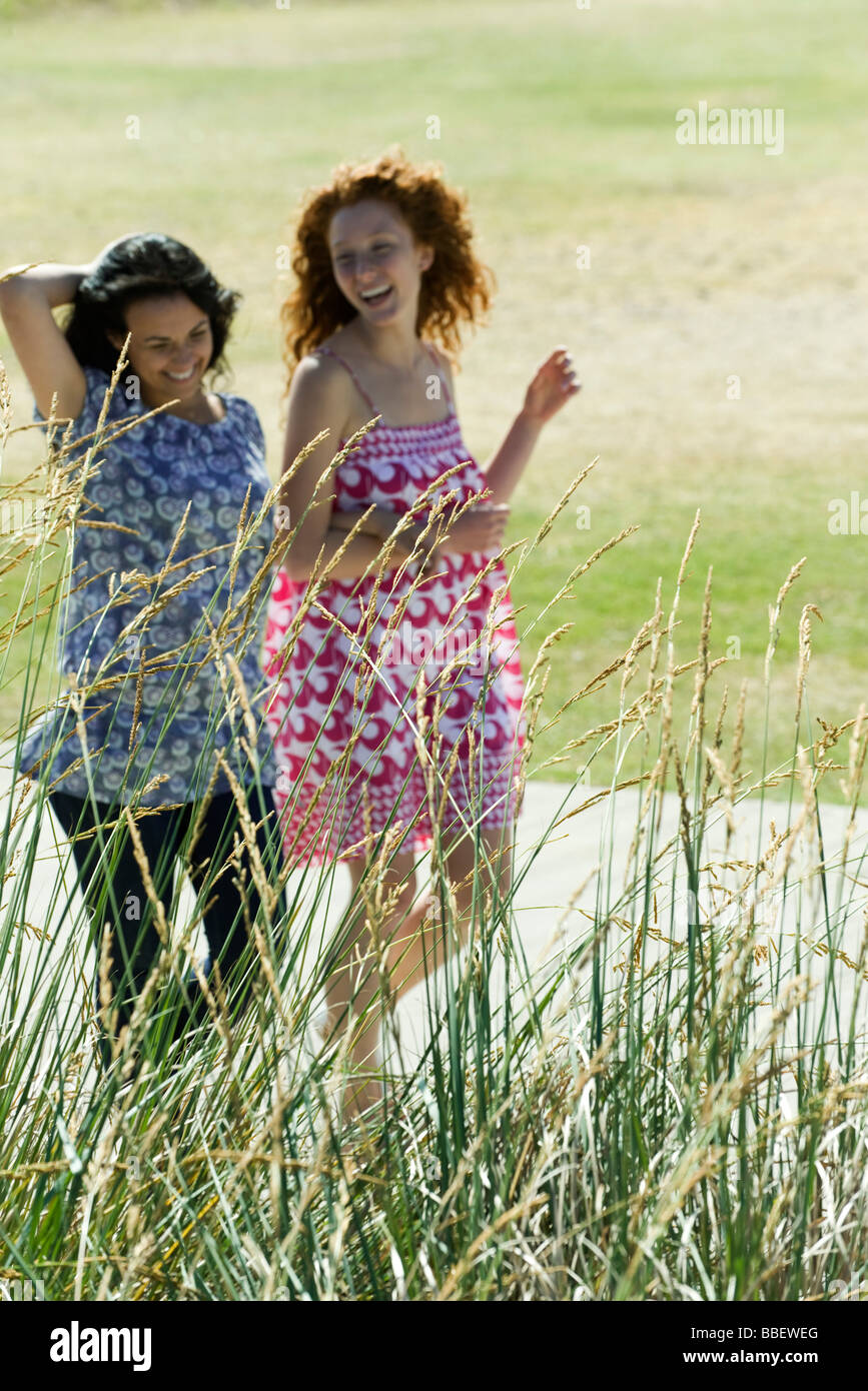 Two young women walking arm in arm outdoors, both laughing Stock Photo