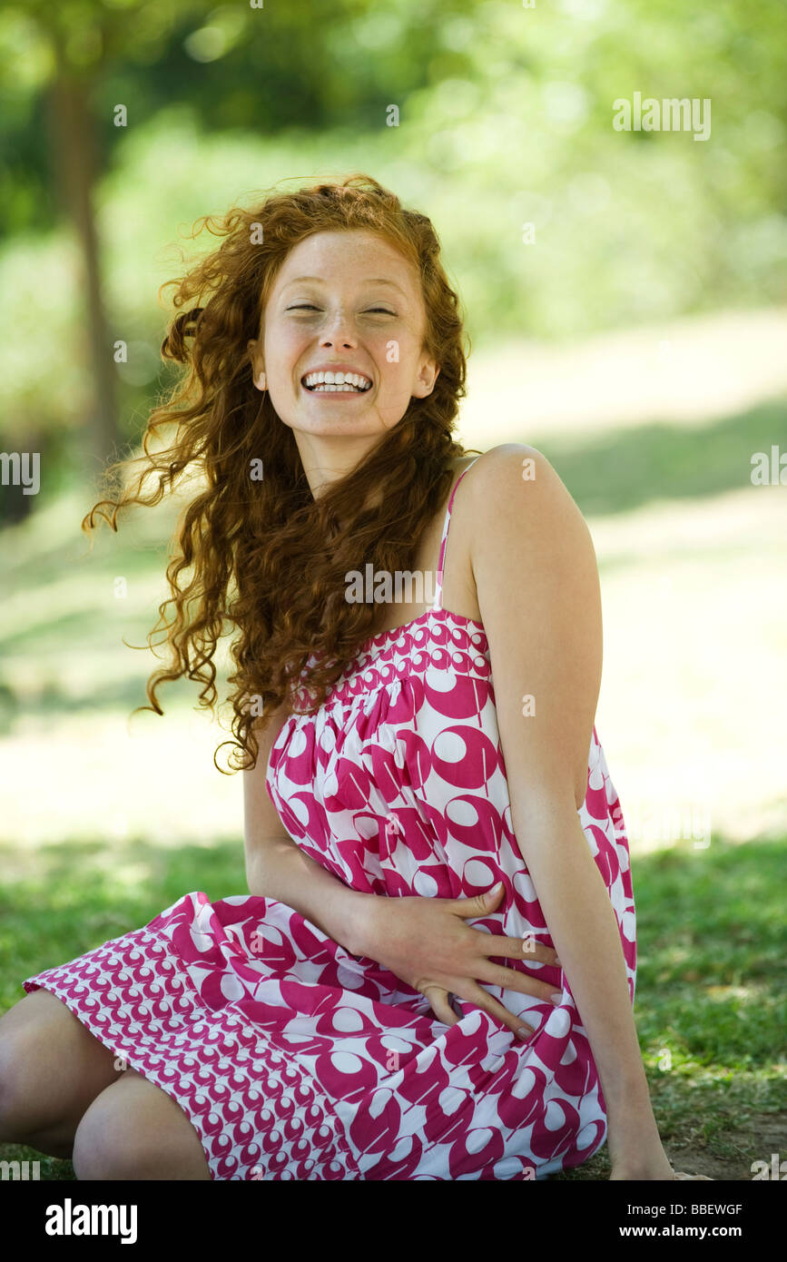 Young red haired woman sitting outdoors, laughing, portrait Stock Photo