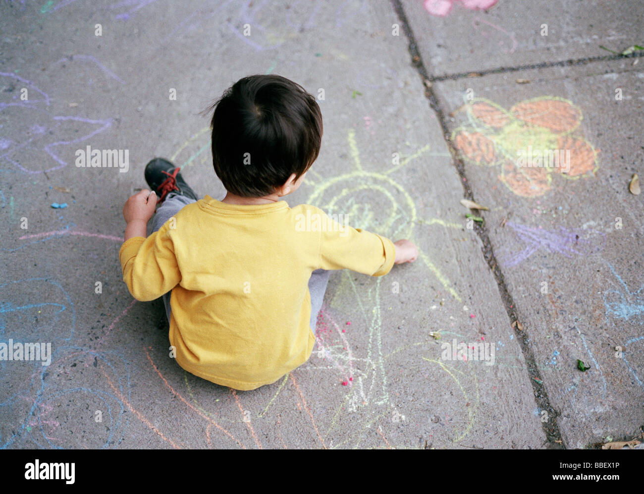 Two year old boy drawing with colorful chalk on a sidewalk Stock Photo ...