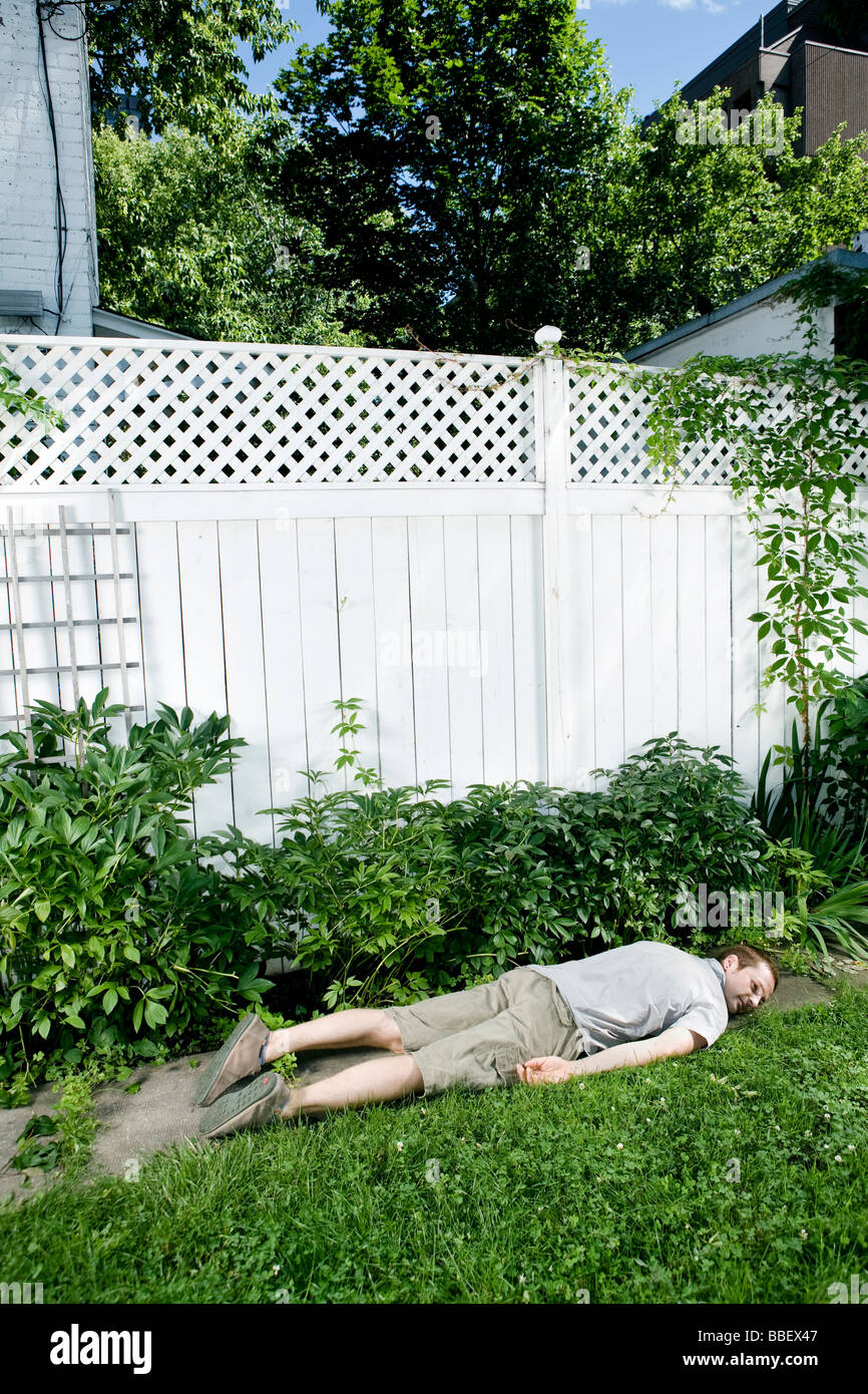 Man laying on a walkway in a backyard in front of a white picket fence, Montreal, Quebec Stock Photo
