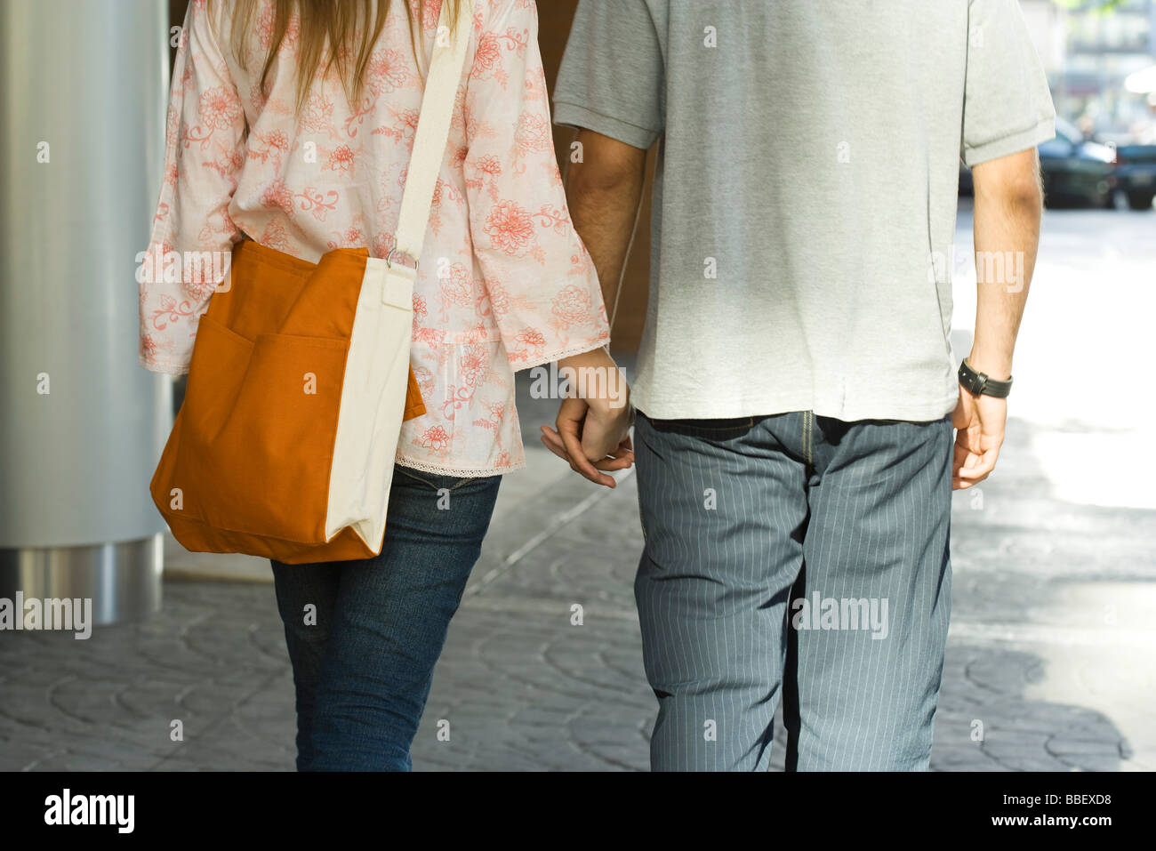 Young couple walking hand in hand on sidewalk, rear view, cropped Stock ...