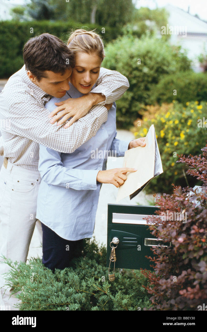 Couple checking mail together, man embracing woman from behind Stock Photo