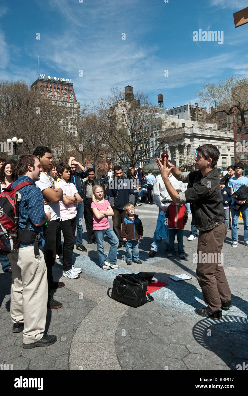 a crowd of young adults & children gather to watch a young man performing sleight of hand in Union Square park, New York City Stock Photo