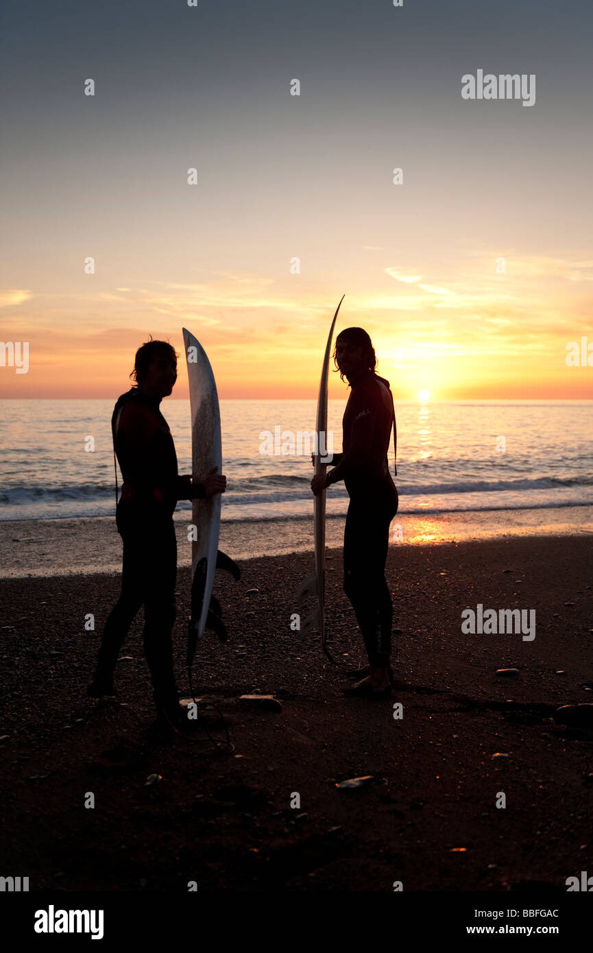 Two young men holding their surf boards about to go  surfing at sunset off Aberystwyth beach Wales UK Stock Photo