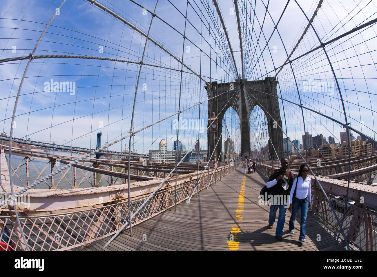 Tourists and New Yorkers pedestrians enjoy walking in sunshine on Brooklyn Bridge Lower Manhattan New York City NYC USA Stock Photo