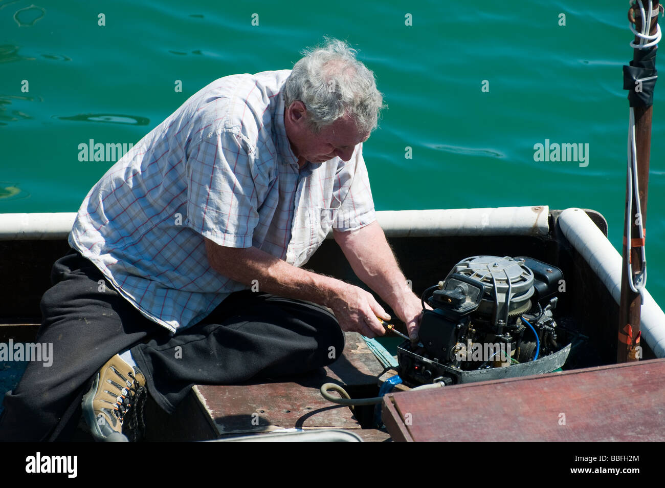 A fisherman repairing the outboard engine on his small fishing boat. Stock Photo