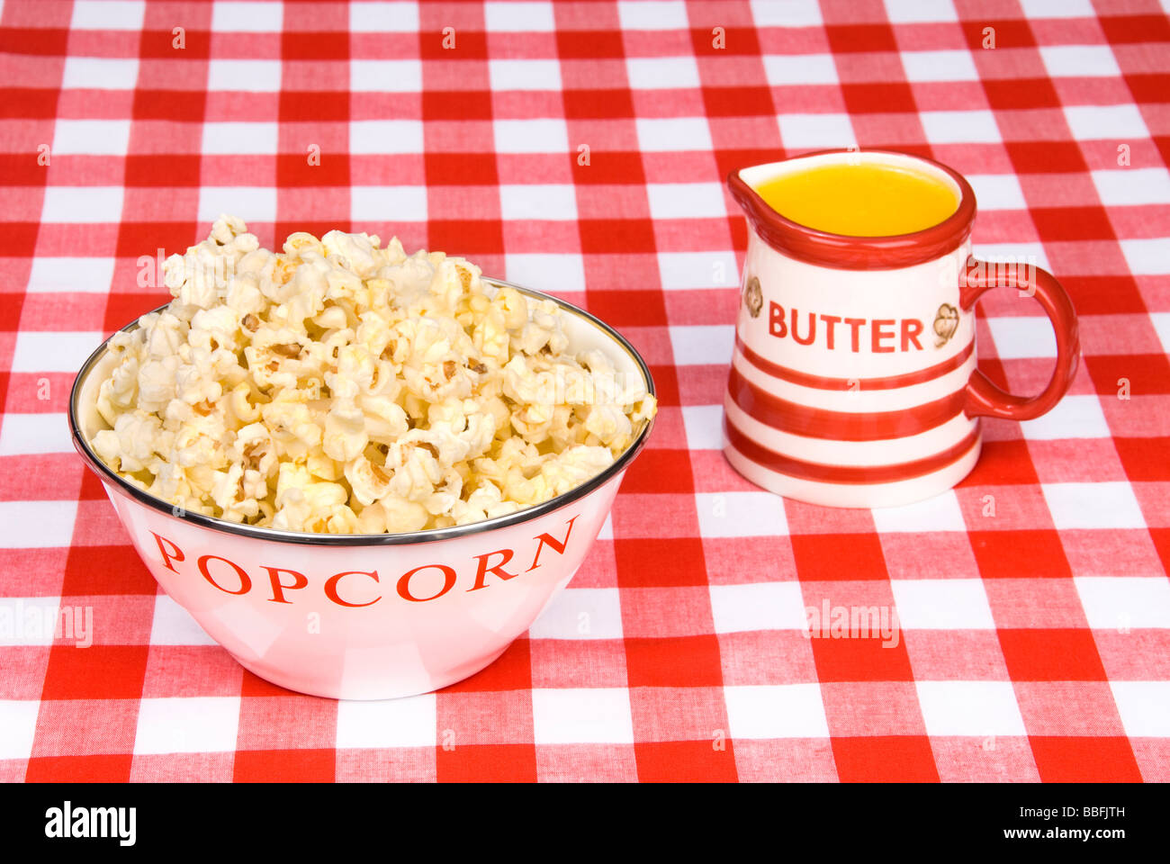 A bowl of hot freshly popped popcorn and a cup of melted butter on a red and white checkered table cloth Stock Photo
