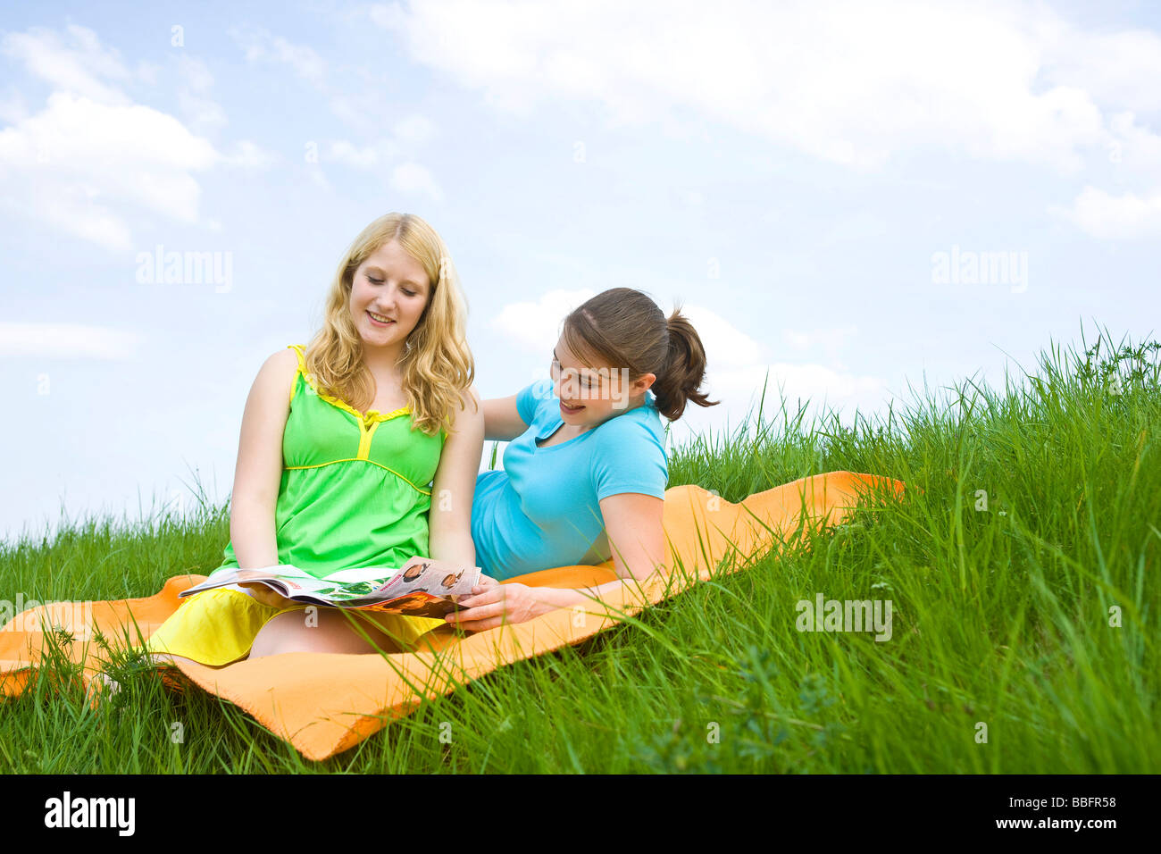 Two smiling girls on a blanket in the grass Stock Photo - Alamy