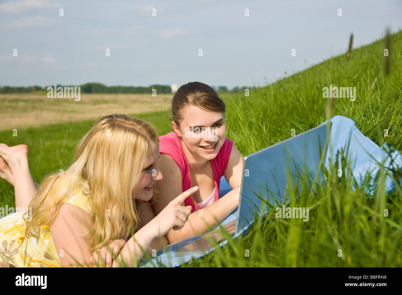 Two smiling girls using a laptop while lying on a blanket on a meadow Stock Photo Alamy