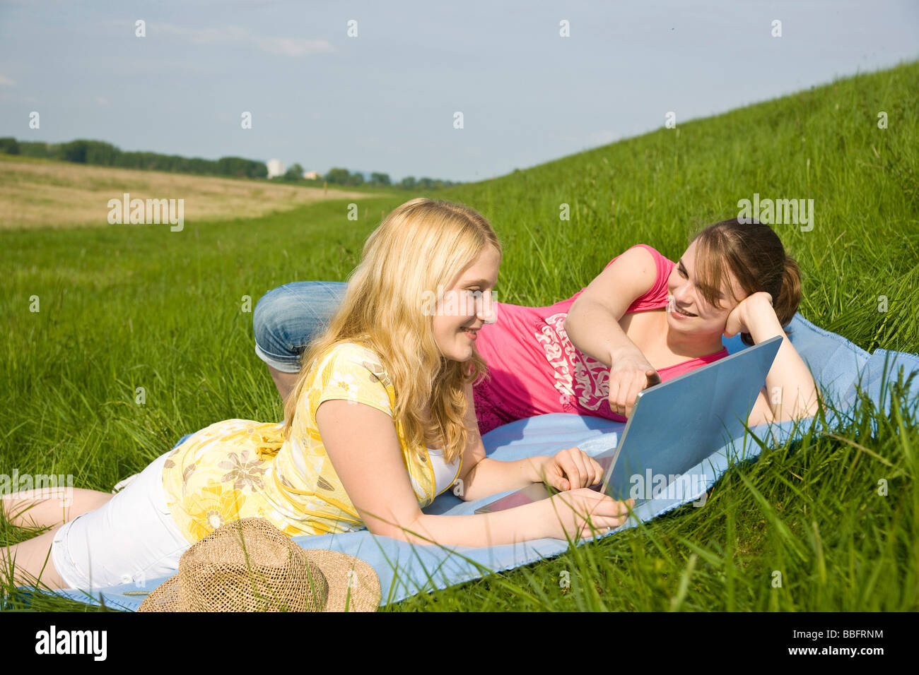 Two smiling girls using a laptop while lying on a blanket on a meadow Stock Photo Alamy